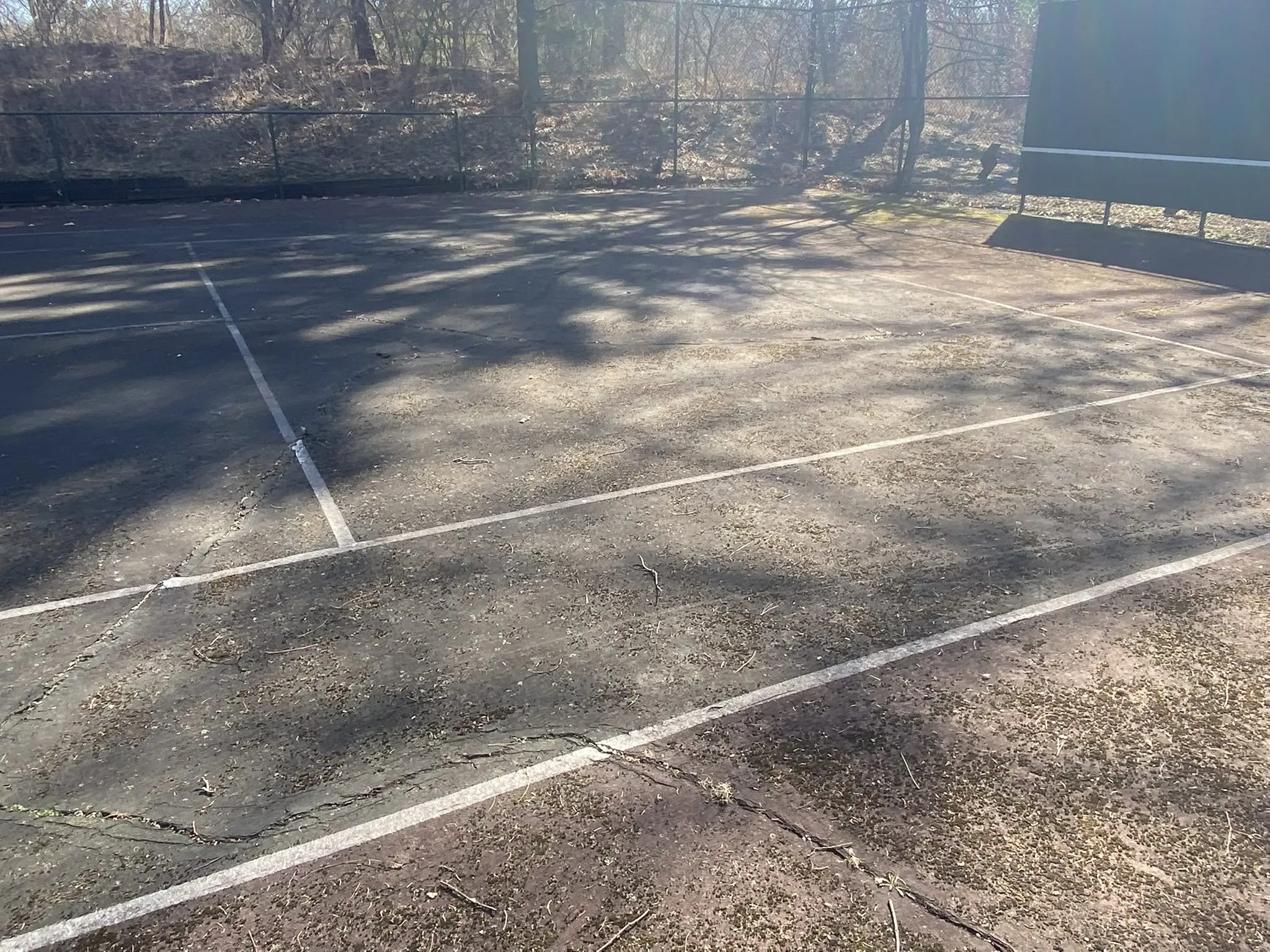 Worn sunlit outdoor tennis court with shadows