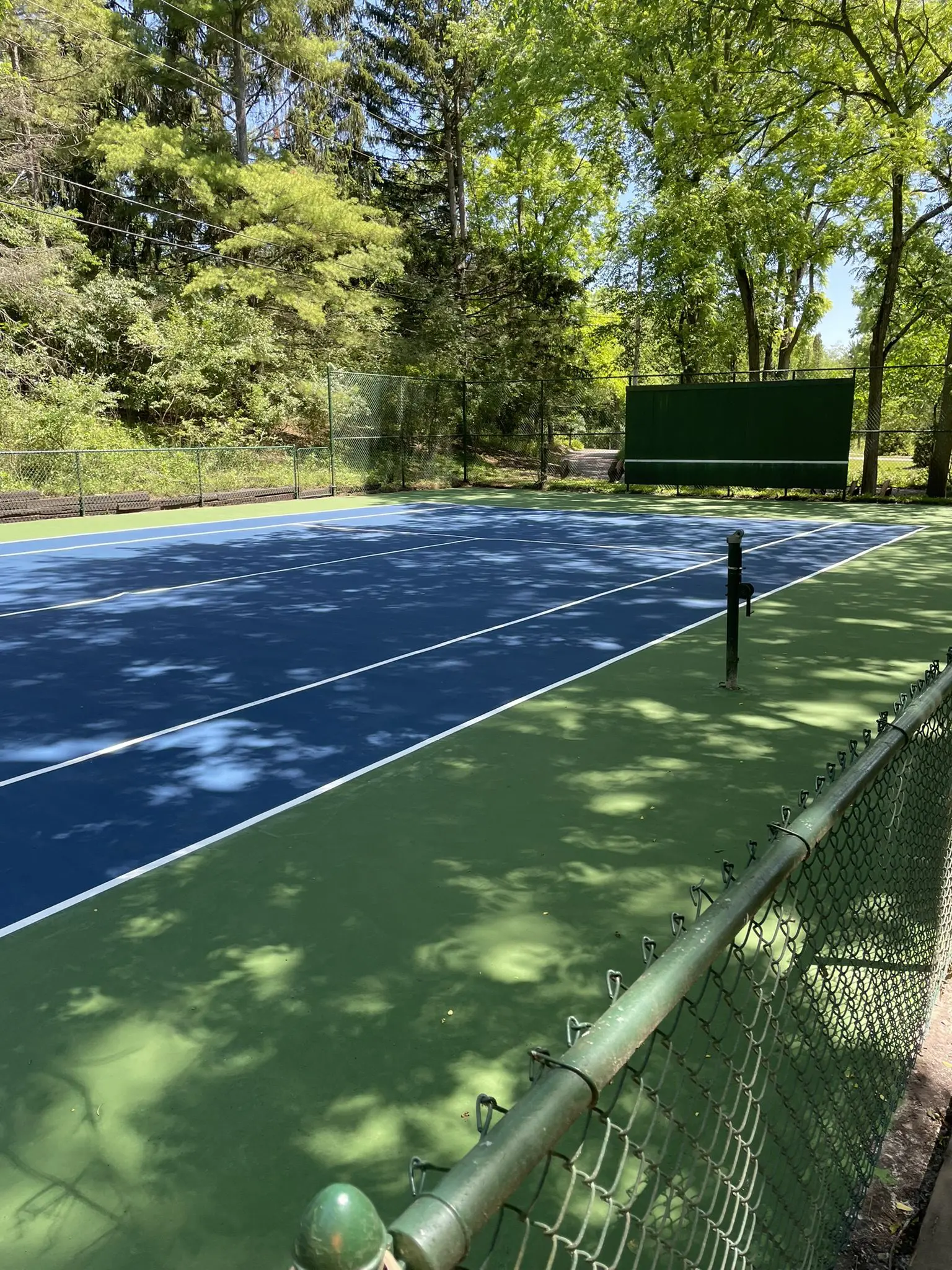 Outdoor blue tennis court with surrounding trees