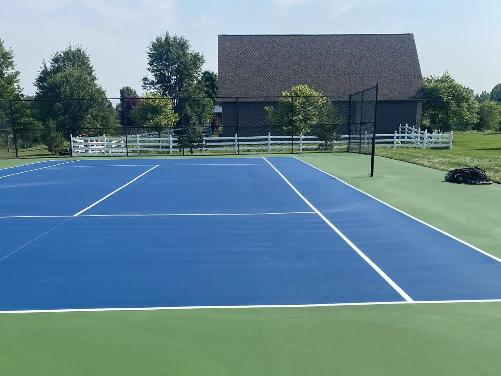 Blue tennis court with barn and fence